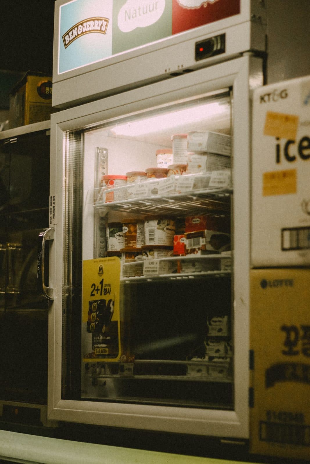 A lit ice cream freezer in a corner shop at night